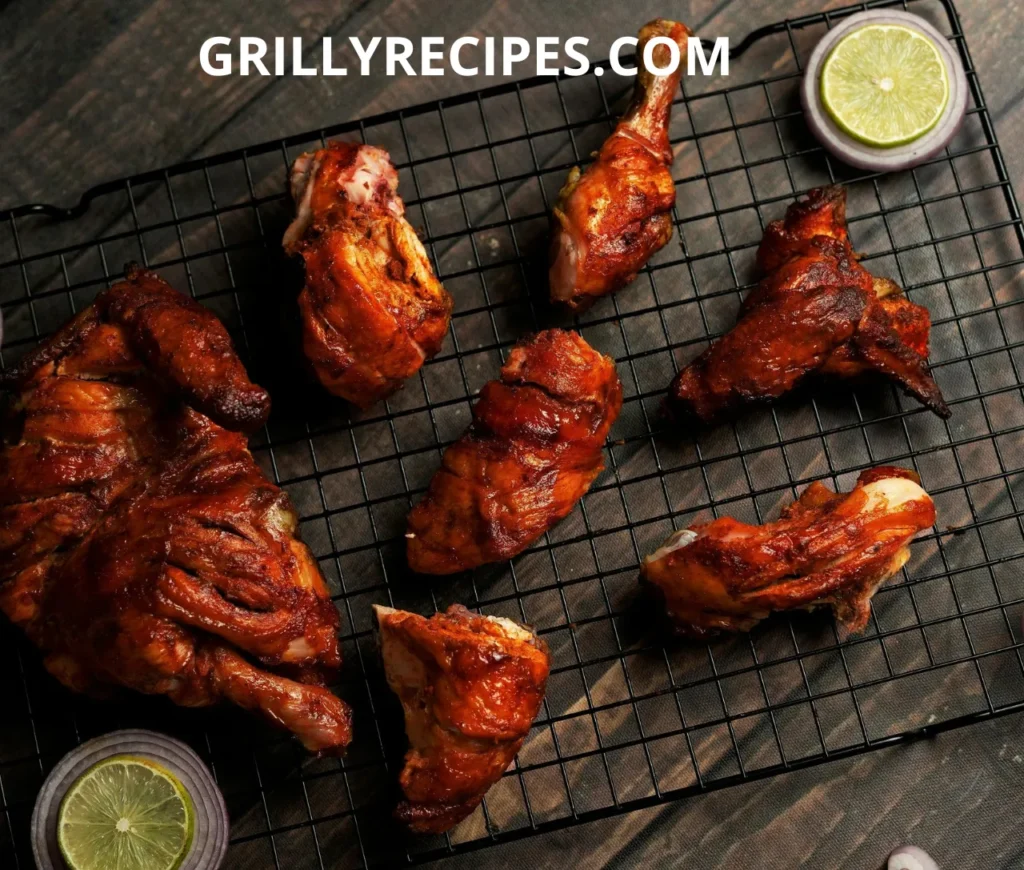 Grilled chicken pieces with a golden-brown crust on a black wire rack, garnished with lime and onion slices.