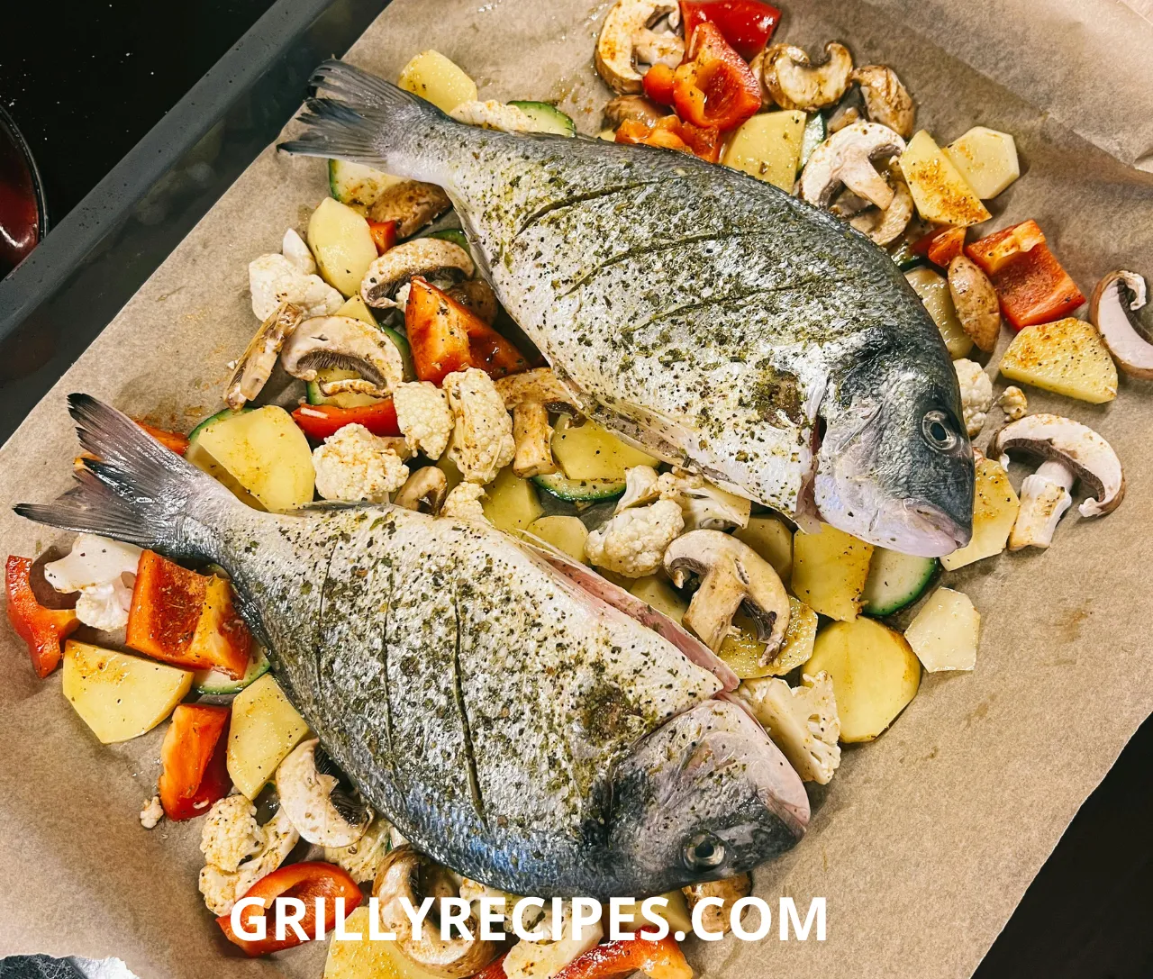 Whole seasoned dorado fish prepared on a baking tray with mixed vegetables, including potatoes, mushrooms, and bell peppers.