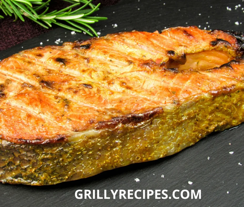 Grilled Dolphin Fish with golden crispy skin, garnished with rosemary on a black slate plate.