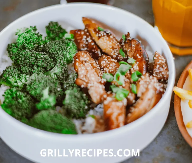 A colorful bowl of chicken broccoli salad featuring shredded chicken, bright green broccoli florets, red onions, cranberries, and sunflower seeds, drizzled with a creamy dressing, served on a white table with a fork.
