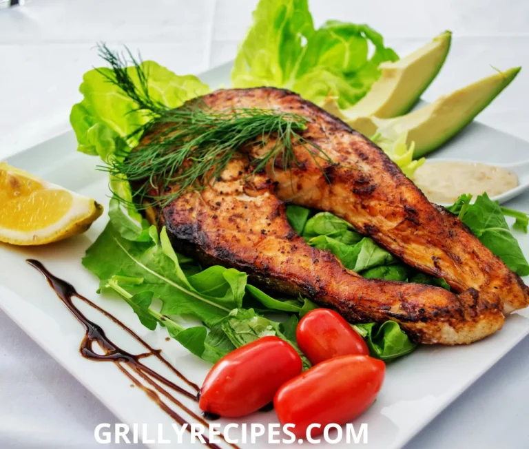 Grilled salmon steak served on fresh green lettuce with cherry tomatoes, avocado slices, lemon wedge, and balsamic glaze drizzle.
