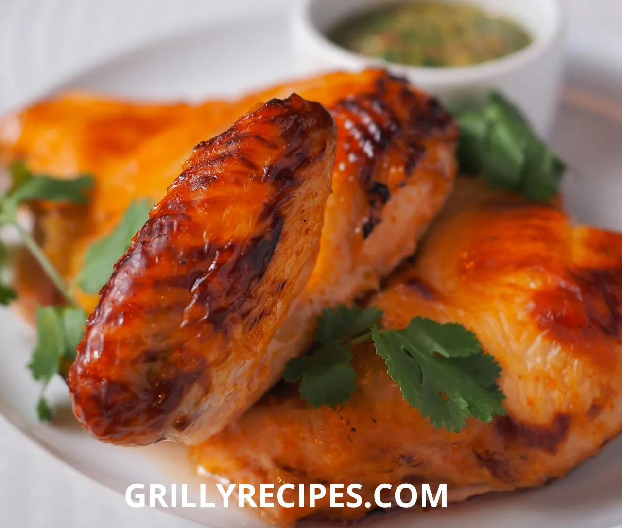 Juicy grilled chicken wings with a golden-brown char, served with dipping sauce on a wooden plate.
