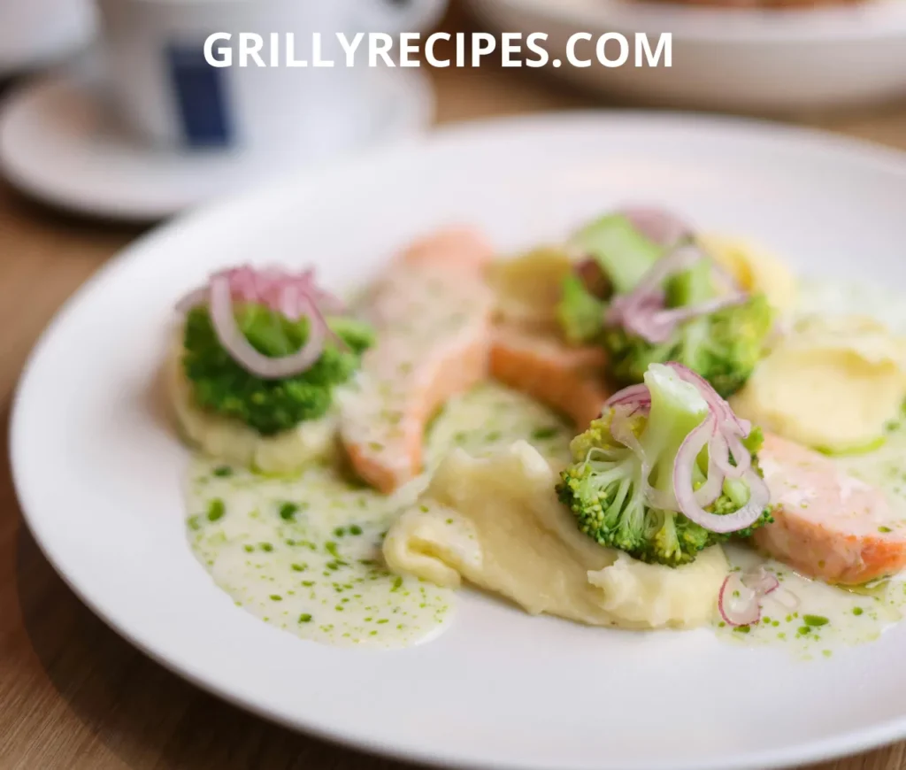 A plated dish of salmon fillet with mashed potatoes, broccoli, red onions, and a creamy herb sauce.