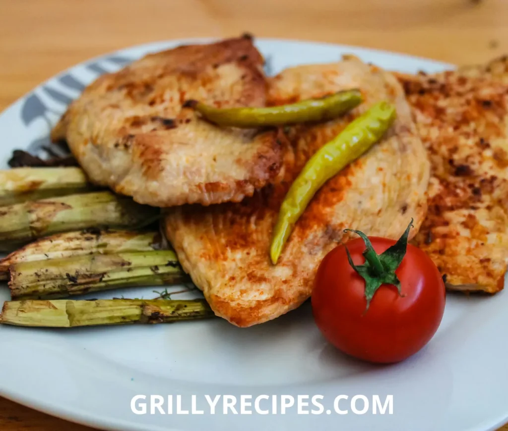 grilled turkey breast  served with asparagus, chili peppers, and a fresh tomato on a white plate.