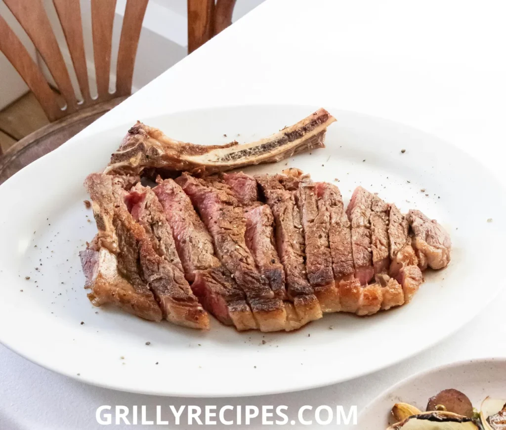  Perfectly grilled tomahawk steak sliced and served on a white plate.