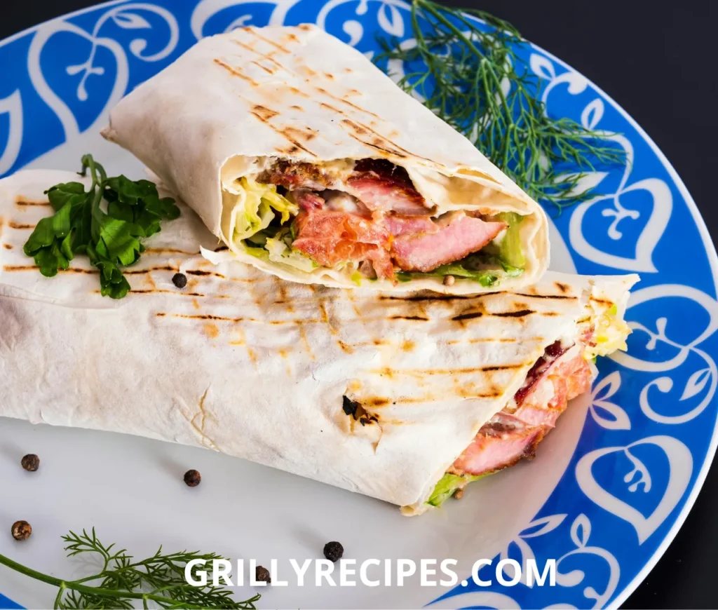 A grilled wrap filled with juicy meat, fresh lettuce, and sauce, served on a decorative blue plate with herbs.

