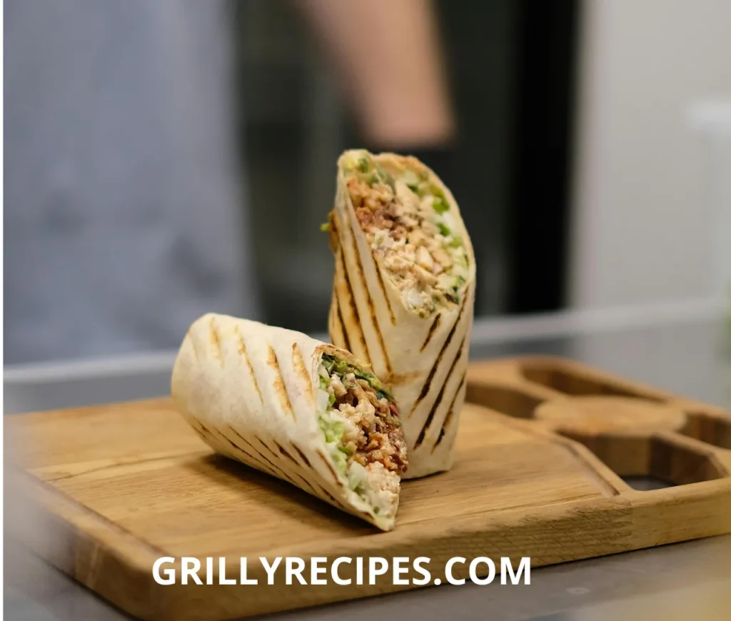 A grilled chicken wrap, sliced in half, revealing a filling of tender chicken, fresh lettuce, and sauce, served on a wooden board.

