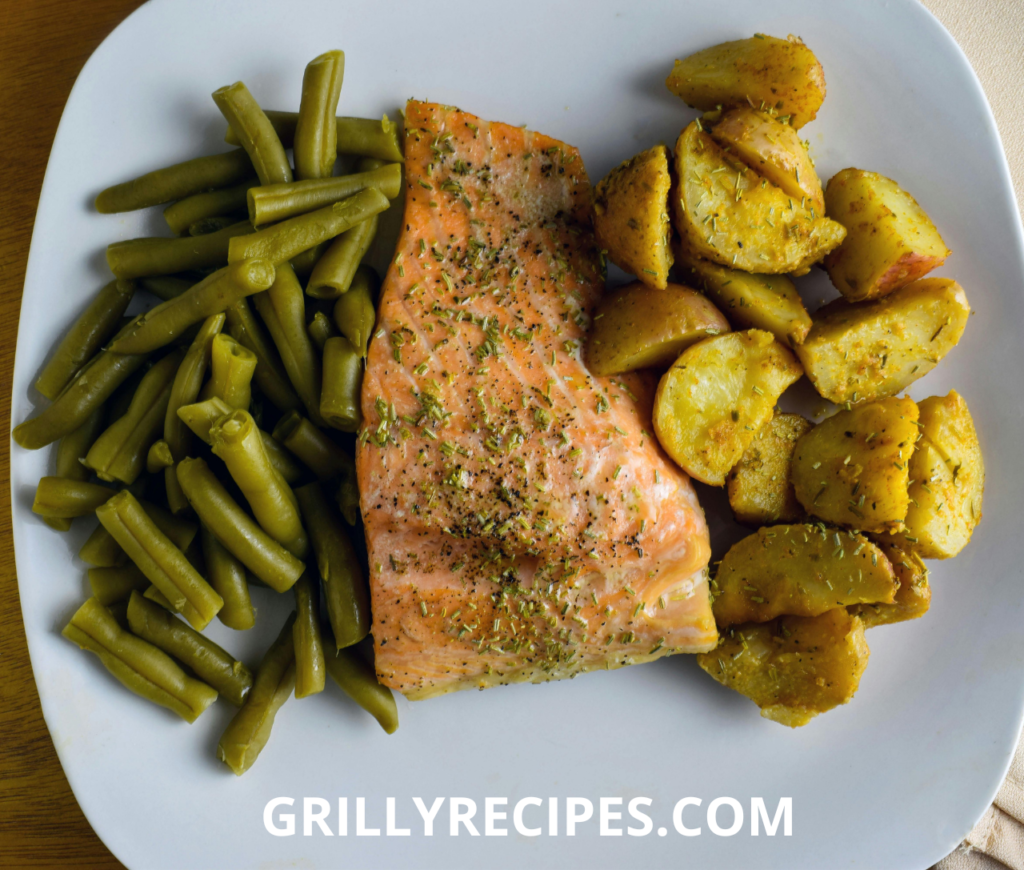 A plate of seasoned salmon with roasted potatoes and green beans.